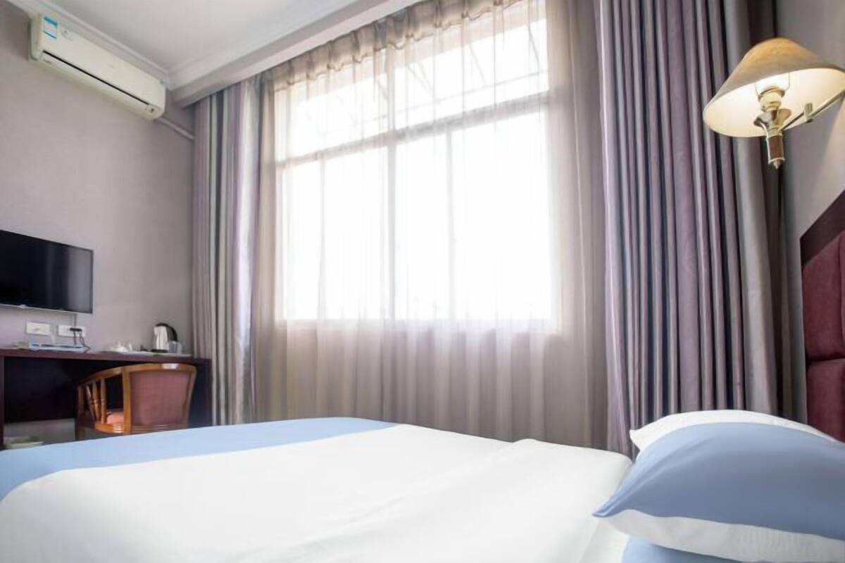 Una habitación de hotel con cama, escritorio, silla, televisor y ventana con cortinas.