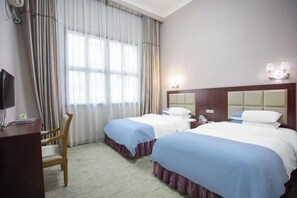 A hotel room with two beds, a desk, a chair, and a TV.