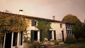 A two-story building with a tiled roof, ivy-covered walls, and multiple windows with shutters.