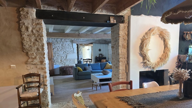 A rustic interior with exposed stone walls, a wooden dining table, and a cozy seating area with a blue sofa.