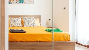 A bed with a yellow bedspread, two floral pillows, a green towel, and a wooden headboard. - Villa Vespucci - Pet Friendly (Montesilvano)