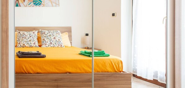 Uma cama com colcha amarela, duas almofadas florais, uma toalha verde e cabeceira de madeira.