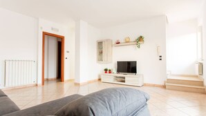 A living room with a TV, a sofa, a staircase, and a door leading to another room. - Villa Vespucci - Pet Friendly (Montesilvano)