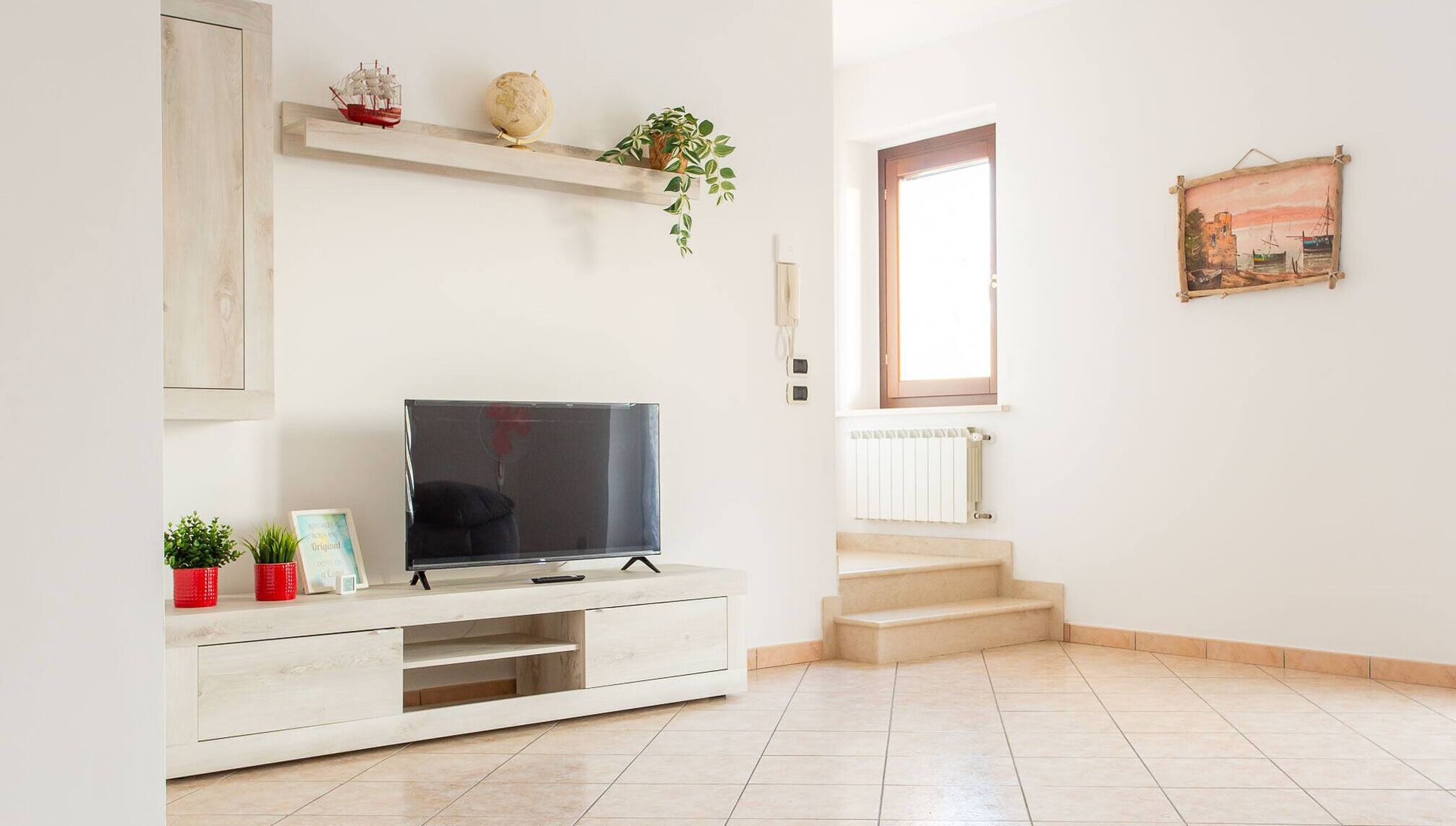 A living room with a TV, a shelf with decorative items, a staircase, and a window.