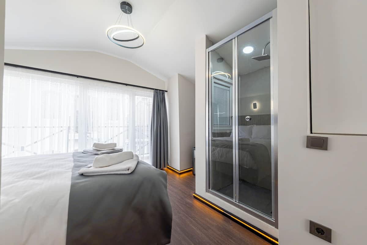 A modern hotel room with a large bed, a walk-in closet, and a large window with curtains.
