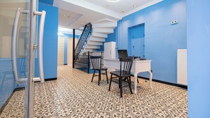 A modern office space with a white desk, two black chairs, a glass partition, a blue wall, a patterned floor, and a staircase. - Ilyada Hotel (Istanbul)