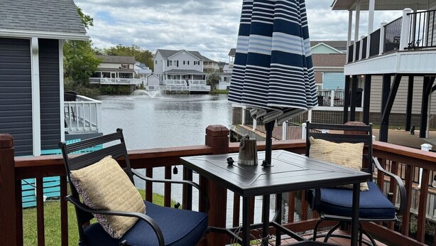 A deck with a table and chairs, overlooking a body of water with houses in the background.