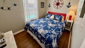 A bedroom with a bed, a ceiling fan, a window with blinds, and nautical-themed wall decorations.