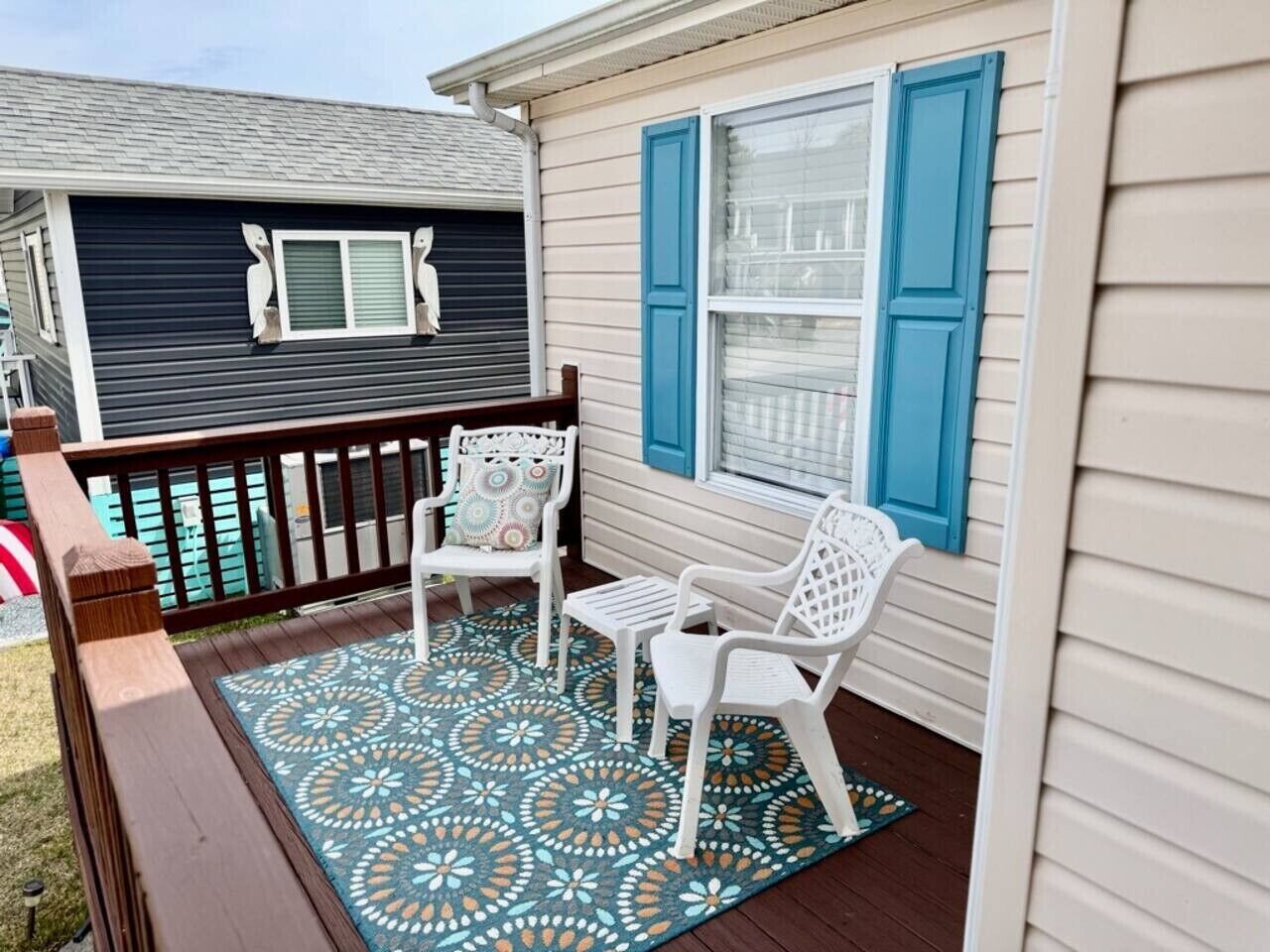 Une véranda couverte avec deux chaises blanches et un tapis à motifs.