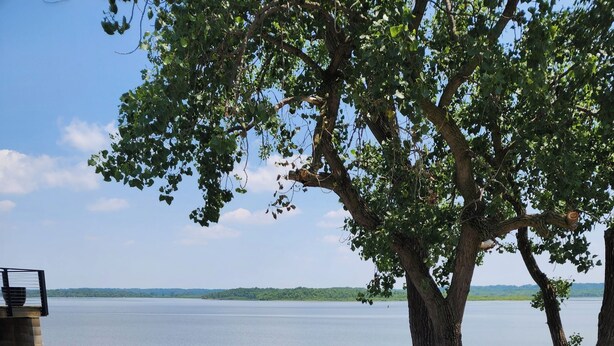 Un área de estar al aire libre con sillas azules y un brasero, con vista a un lago tranquilo.
