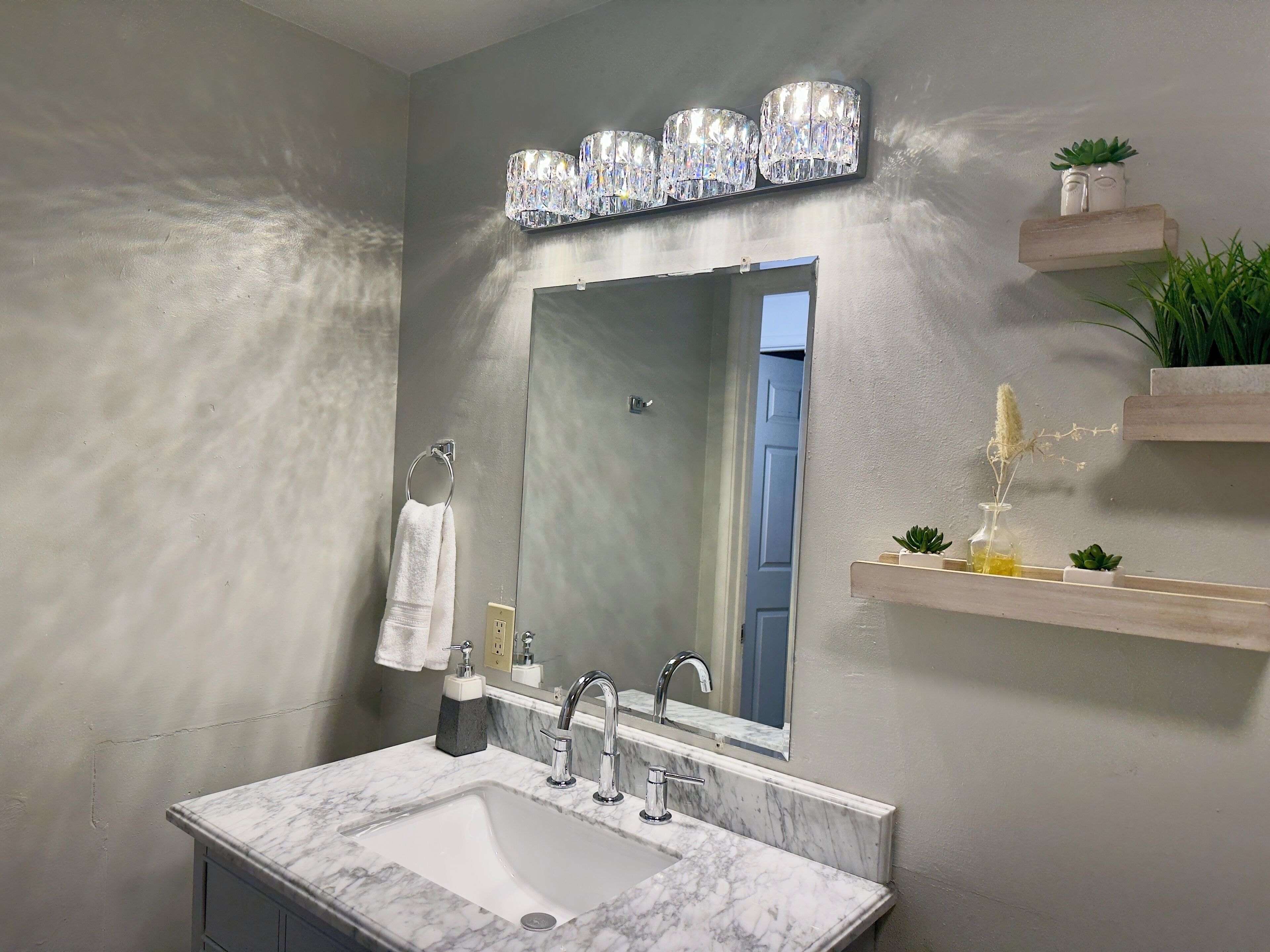 A bathroom with a marble sink, a mirror, a towel rack, and a shelf with plants.