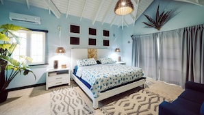 A bedroom with a bed, bedside tables, a potted plant, and a ceiling fan. - Ocean front luxury villa iin gated golf course community with private beach. (Lowlands)