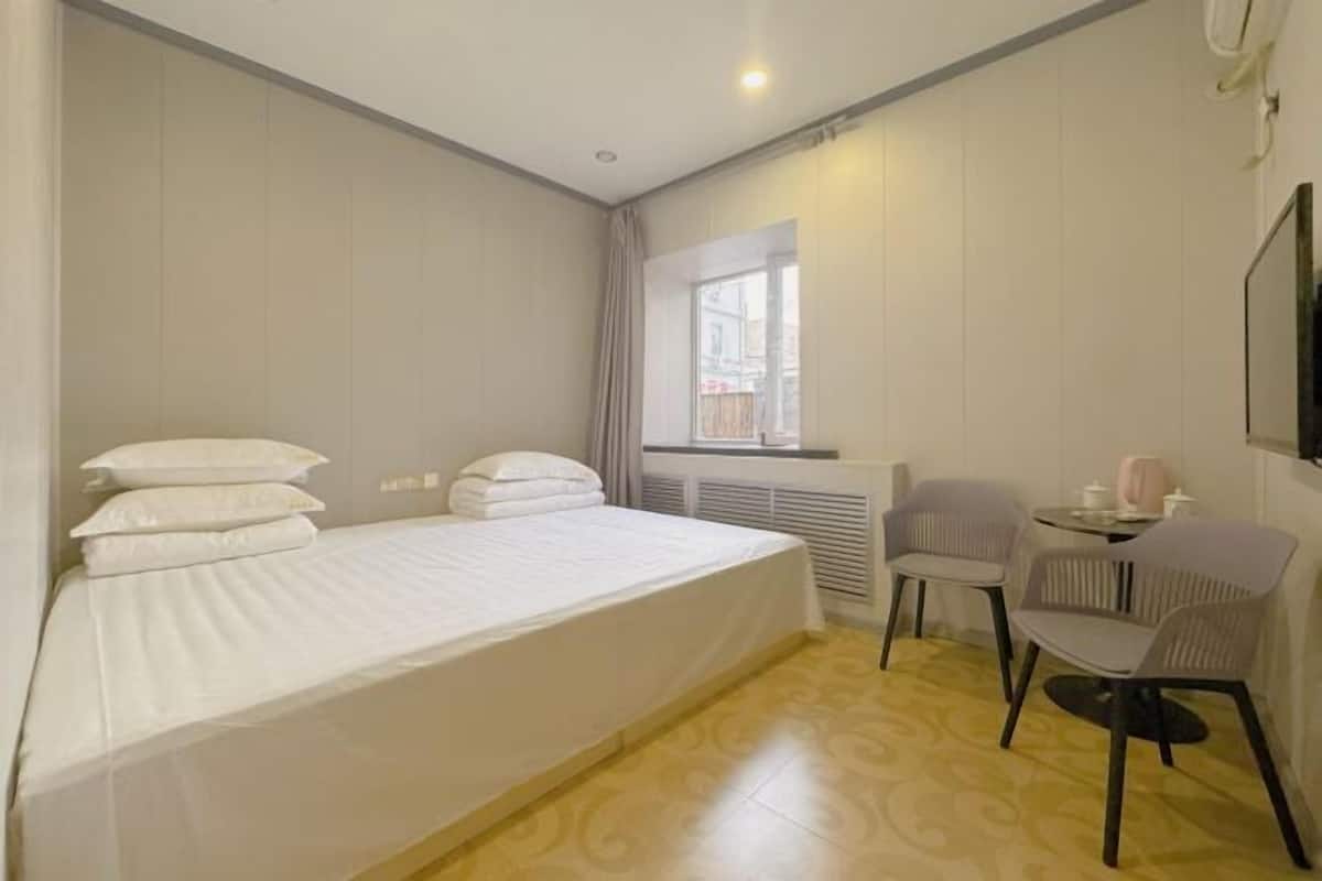 Ein Hotelzimmer mit Bett, Stuhl, kleinem Tisch, Fenster und Heizkörper.