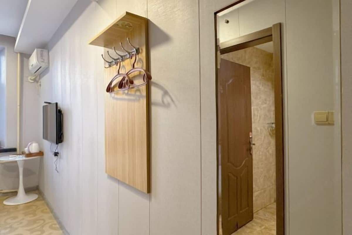 Ein Flur mit einem Holz-Kleiderständer, einem an der Wand befestigten Fernseher und einer Tür zu einem anderen Raum.