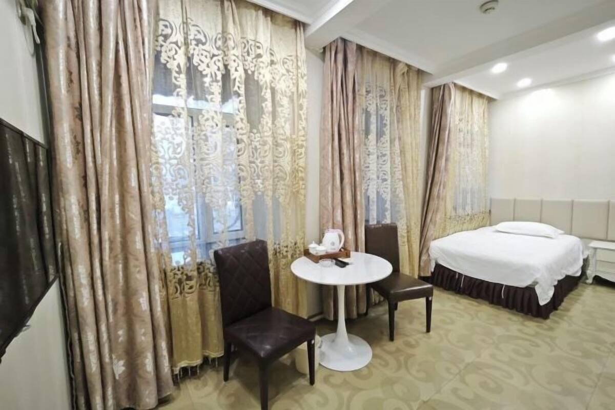 Ein Hotelzimmer mit einem Bett, einem runden Tisch mit zwei Stühlen, einem kleinen Tisch mit einer Dekoration und Vorhängen mit floralem Muster.