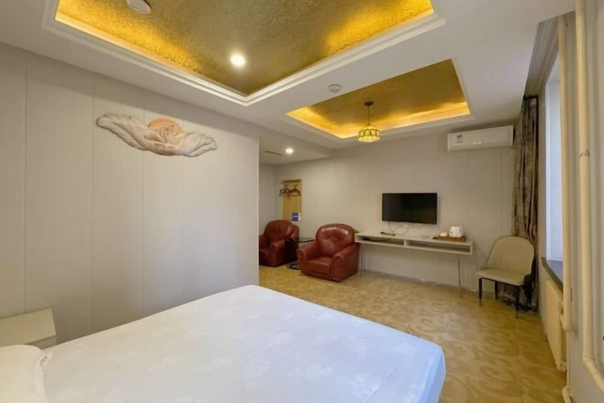 Ein Hotelzimmer mit einem großen Bett, einem Schreibtisch mit Flachbildfernseher, zwei Ledersesseln und einer Decke mit Einbaustrahlern.