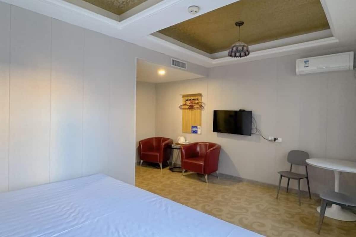 Ein Hotelzimmer mit einem Bett, einem Schreibtisch, zwei roten Stühlen, einem an der Wand montierten Fernseher und einer Klimaanlage.