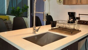 Una cocina moderna con un lavaplatos integrado, armarios de madera, una cafetera y una planta.