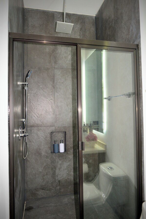 A modern shower with a glass door, a handheld showerhead, and a wall-mounted faucet.
