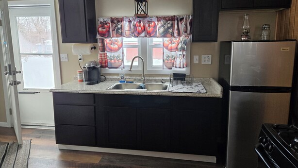 A kitchen with dark cabinets, a stainless steel refrigerator, a sink, and a window with a fruit-themed curtain. - 2-bedroom country house in West Springfield, PA with WiFi, AC (West Springfield)