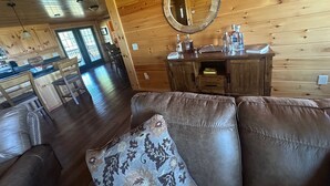 Een gezellig interieur van een chalet met een houten vloer, een leren bank, een houten eettafel en een keukenhoek met een houten kast en een spiegel.