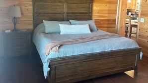 Een slaapkamer met houten lambrisering, een bed, nachtkastje, lamp en plafondventilator.