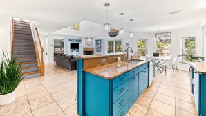 Une cuisine spacieuse avec un îlot central bleu, un coin repas avec une table et des chaises, et un escalier menant à un autre niveau.
