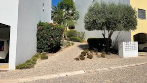 A courtyard with cobblestone paths, a small tree, and a hedge with pink flowers. - The Pomar 2 Bedroom Suite -5 People Terrace Swimming Pools (Tavira)