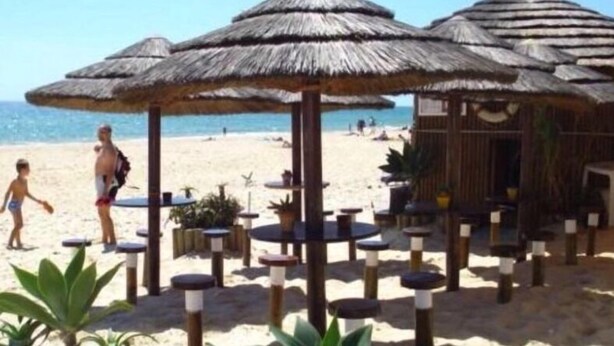 A beachside setting with thatched umbrellas, wooden tables, and potted plants. - The Pomar 2 Bedroom Suite -5 People Terrace Swimming Pools (Tavira)