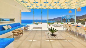 Una habitación iluminada por el sol, con piscina, muebles azules y vista al mar.