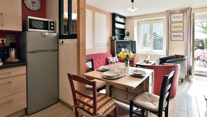 Een kleine keuken met een koelkast, magnetron en een eethoek met stoelen en een tafel.