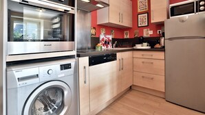 Een kleine keuken met een wasmachine, een magnetron, een koelkast en houten keukenkastjes.