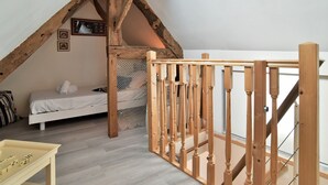 Een slaapkamer met een schuine kap, een houten trap, een bed en een klein tafeltje met dobbelstenen.
