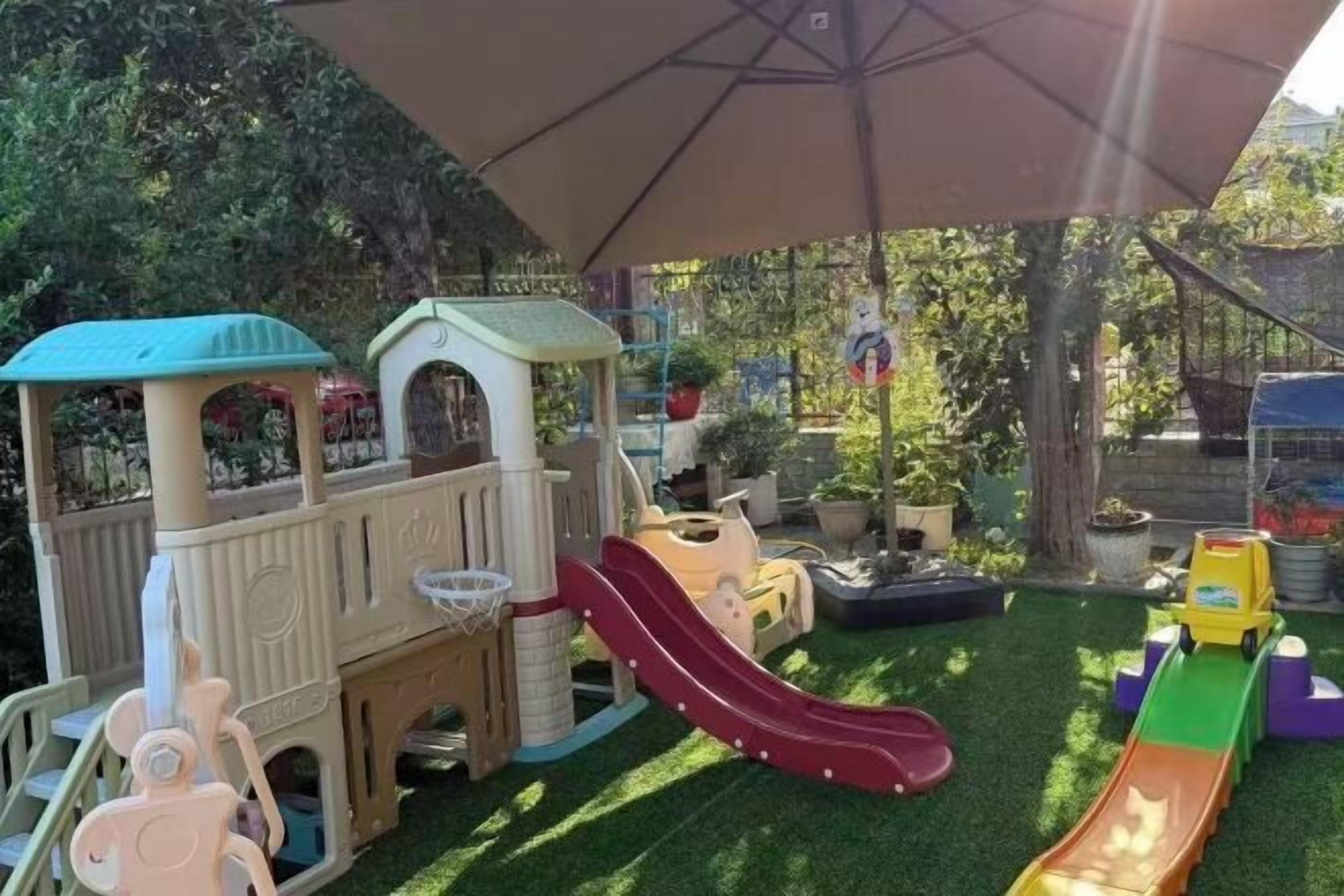 Un espace de jeux pour enfants avec un toboggan, des structures d’escalade et un petit panier de basket.