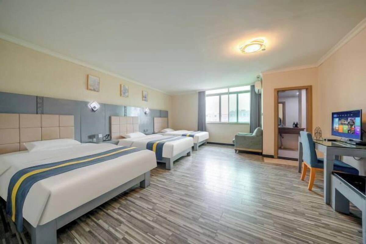 Una habitación de hotel con tres camas, un escritorio, un televisor y una ventana.