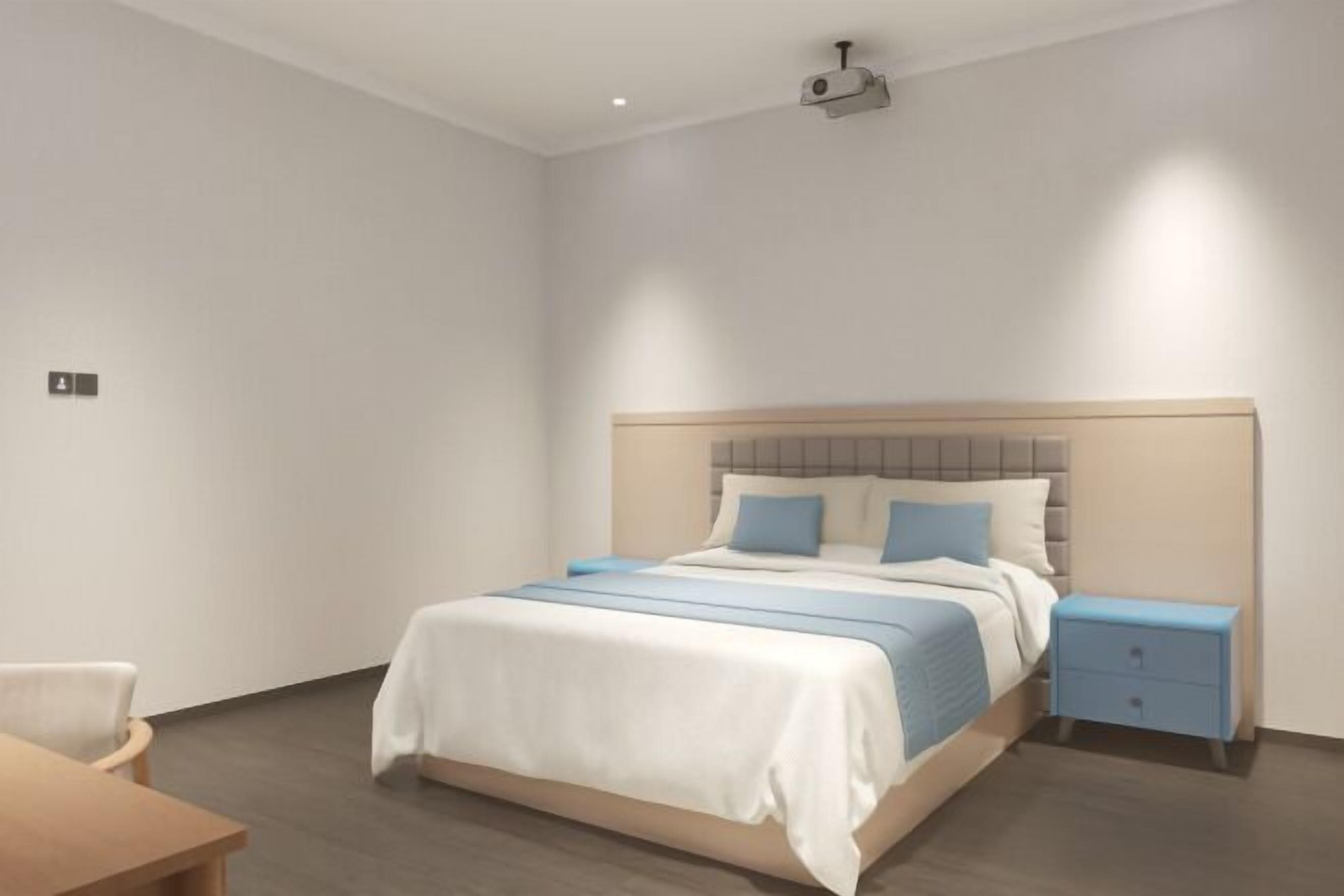 A modern bedroom with a bed, bedside table, and a projector mounted on the ceiling.