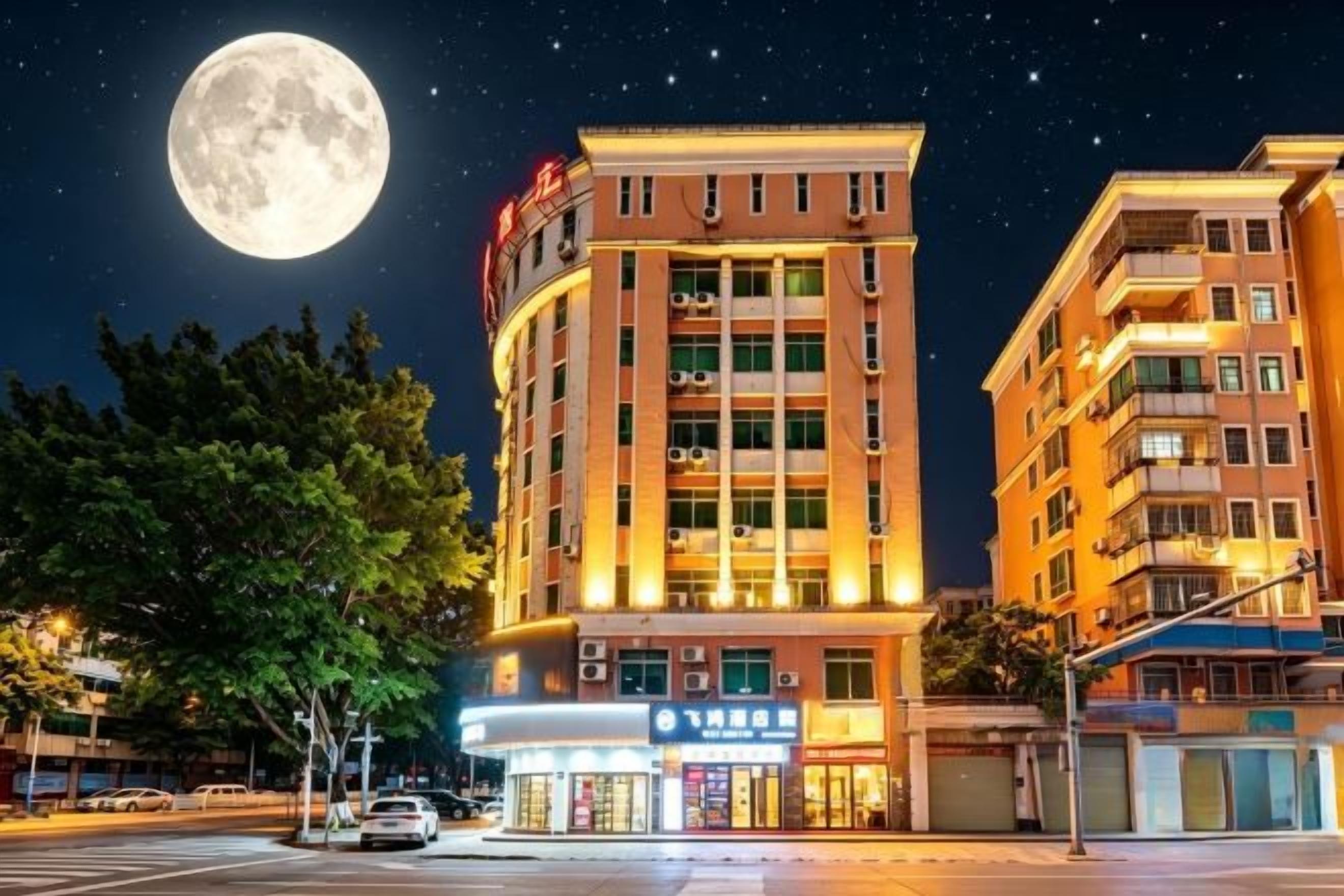 Um edifício de hotel com vários andares, sinalização iluminada e uma grande lua no céu.