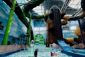 Parque acuático interior con toboganes, una piscina grande y un mural con temática tropical.