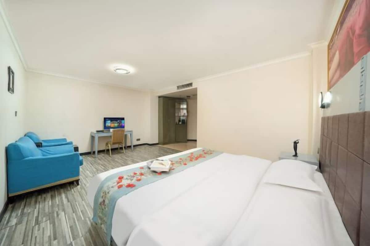 Una habitación de hotel con cama, sofá azul, escritorio y televisión.