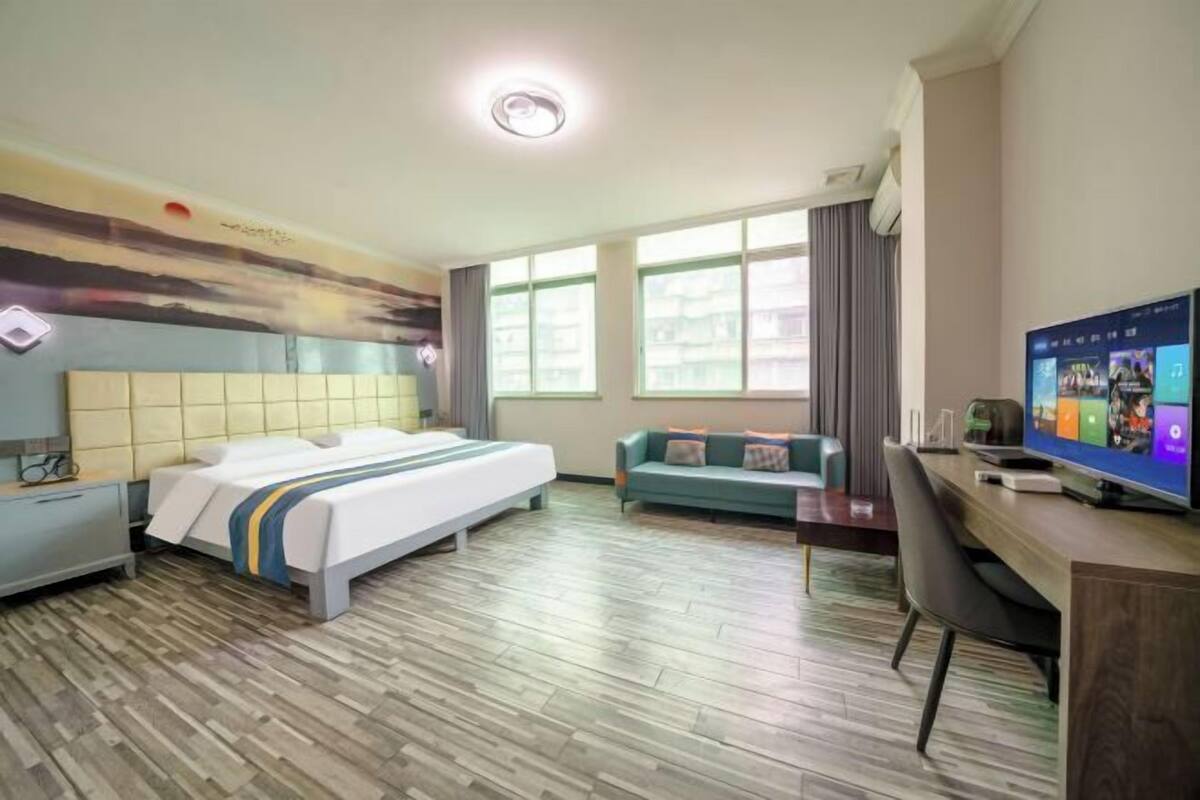 Habitación de hotel con cama, sofá, escritorio, televisor y ventanas amplias.