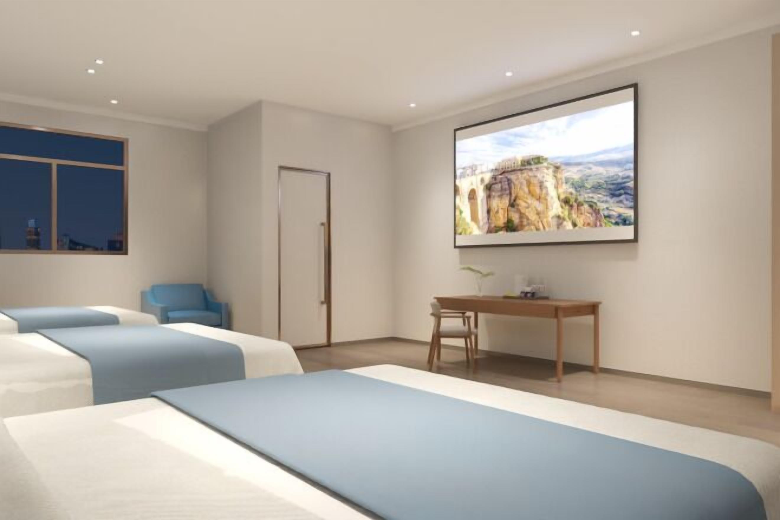 Een hotelkamer met drie bedden, een bureau, een stoel en een groot raam.