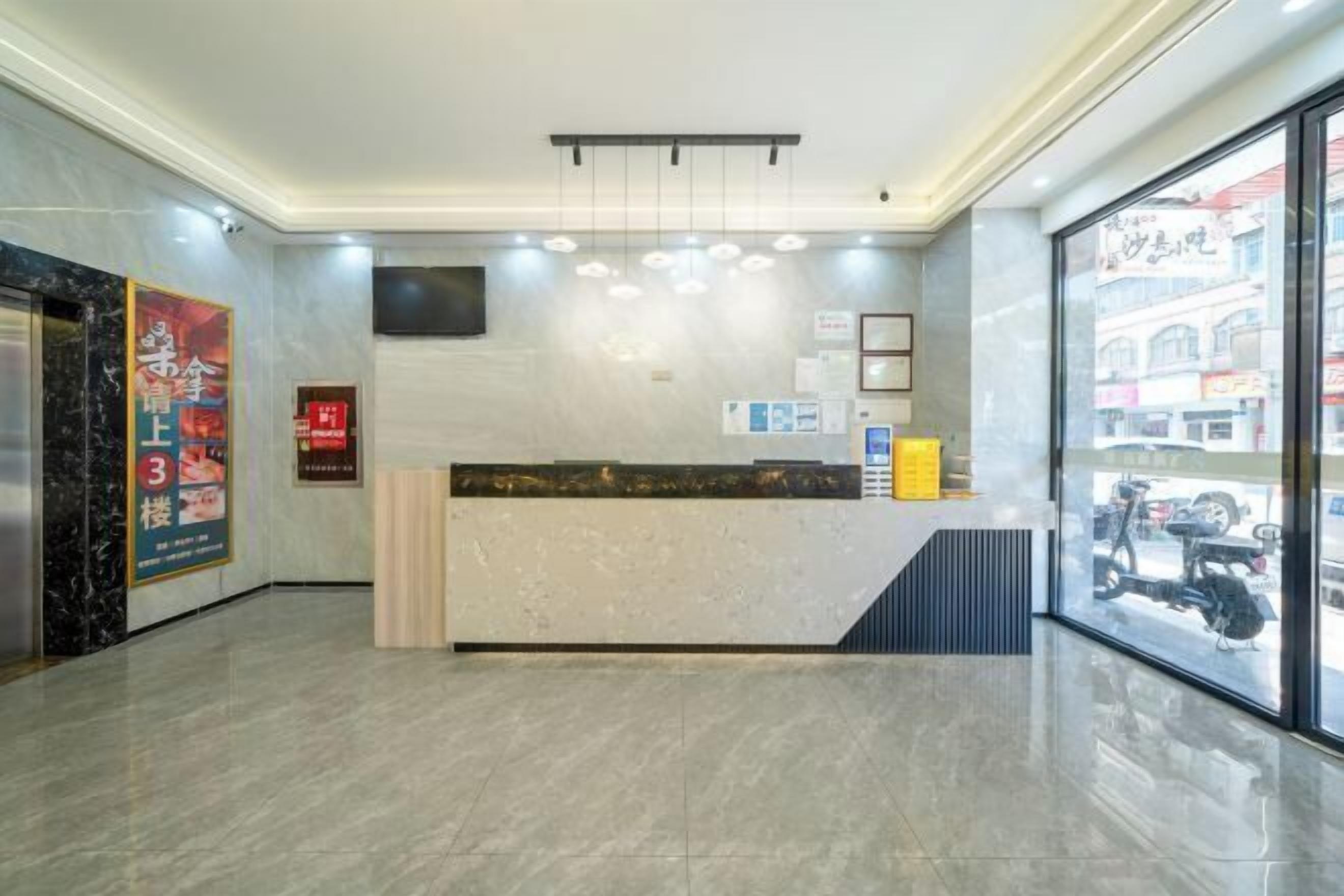 A hotel reception area with a marble floor, a reception desk, a flat-screen TV, and a large window offering a view of the street.