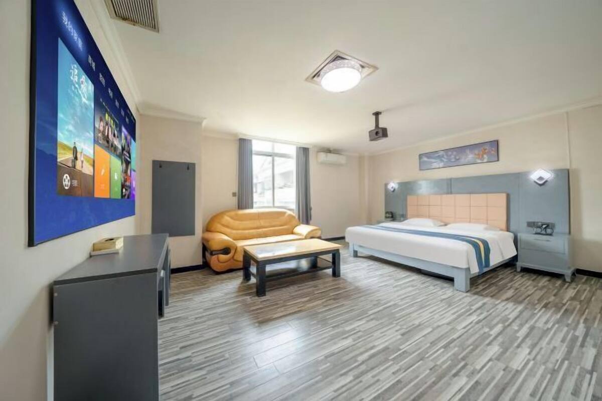 Una habitación de hotel con cama, sofá, escritorio y televisor montado en la pared.