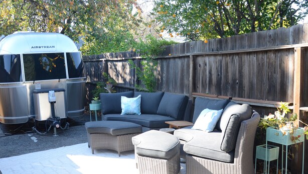 A backyard with a sectional sofa, two ottomans, a small table, and a portable grill. - Cozy airstream escape, hot tub & lights (Concord)