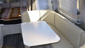 A compact RV interior with a white table, beige seating, and a patterned blanket on the couch. - Cozy airstream escape, hot tub & lights (Concord)
