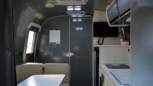 A compact RV interior with a kitchenette, a dining area, and a whiteboard with a message. - Cozy airstream escape, hot tub & lights (Concord)