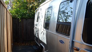 A vintage camper van parked in a narrow space with a wooden fence and trees in the background. - Cozy airstream escape, hot tub & lights (Concord)