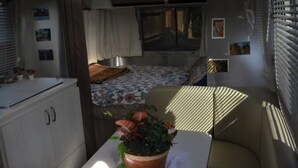 A compact RV interior with a kitchenette, a bed with a floral bedspread, and a potted plant on a table. - Cozy airstream escape, hot tub & lights (Concord)