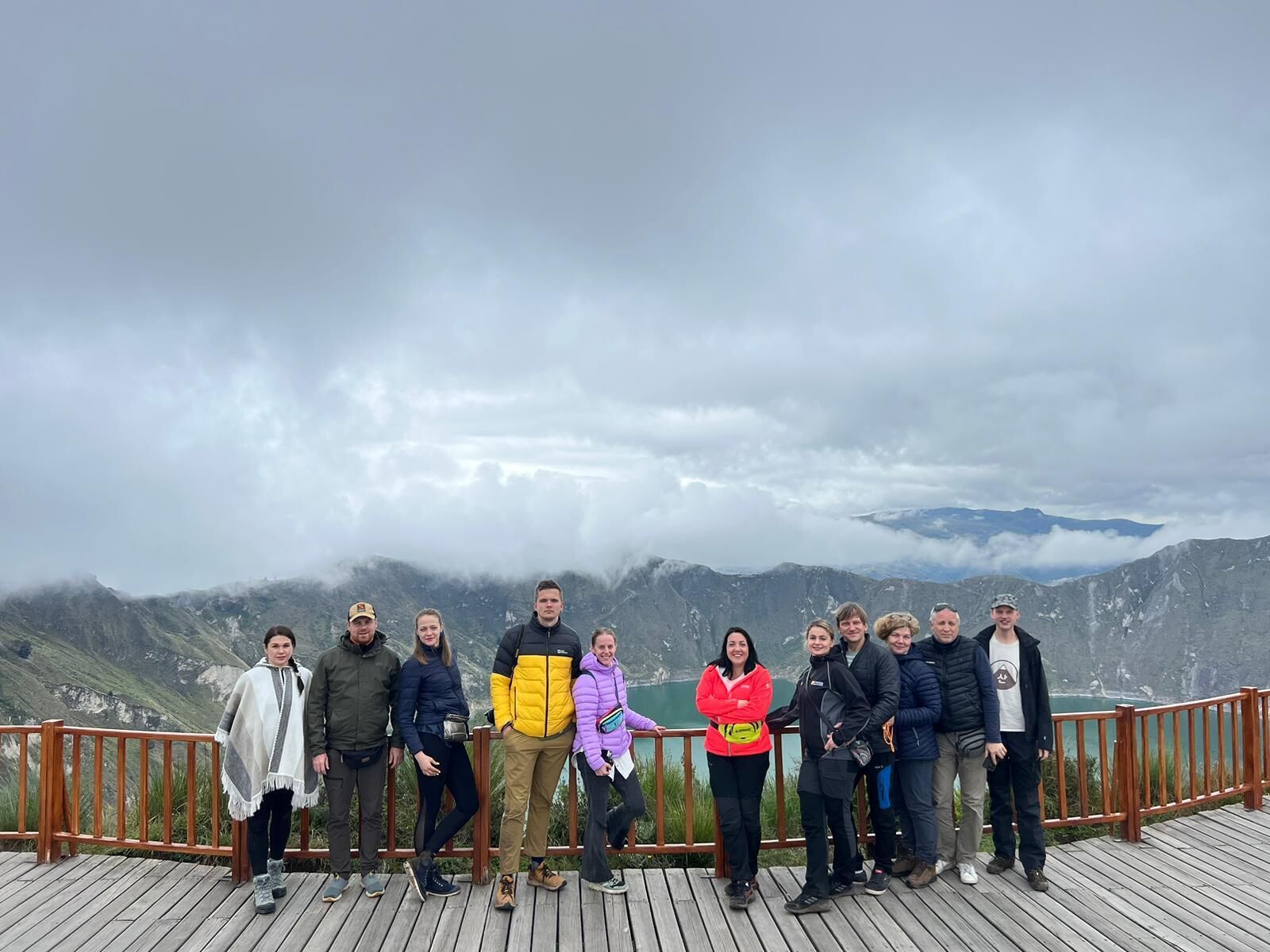 A group of people standing on a wooden deck with a mountainous landscape in the background.