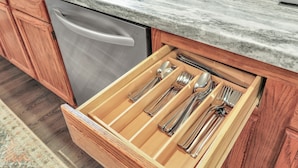 Une cuisine équipée d’un lave-vaisselle en acier inoxydable, de meubles en bois et d’un organiseur de tiroir pour les ustensiles.